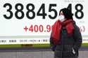 A person walks in front of an electronic stock board showing Japan's Nikkei index at a securities f…